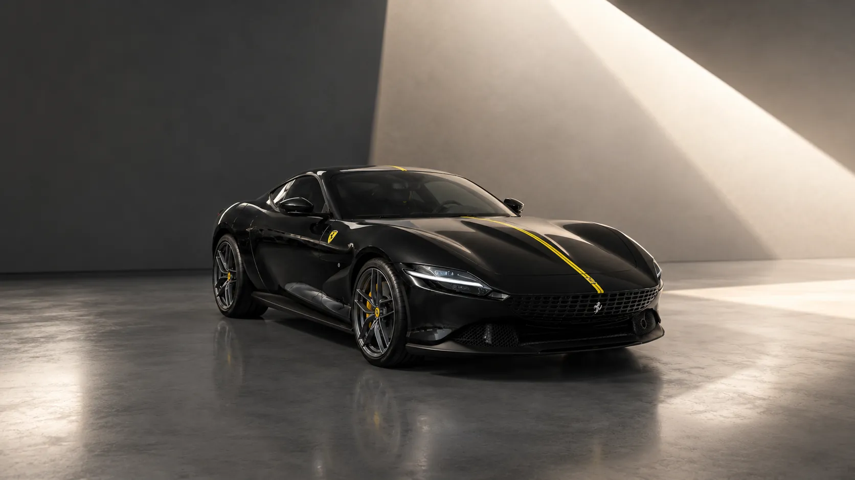 Ferrari Roma nera con fascia gialla, in una sala di cemento attraversata da una lama di luce