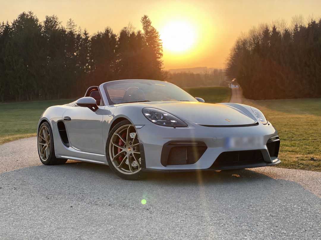 Porsche 718 Spyder grigia, capote aperta, ferma su una strada di campagna al tramonto